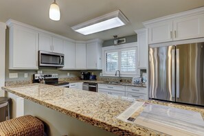 A kitchen with white cabinets, a stainless steel refrigerator, a microwave, a coffee maker, and a granite countertop.