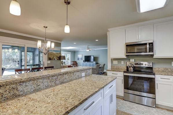 A kitchen with granite countertops, stainless steel appliances, white cabinetry, and a dining area with a view.