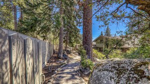 A stone pathway leading through a wooded area with a wooden fence on one side and a house in the background.
