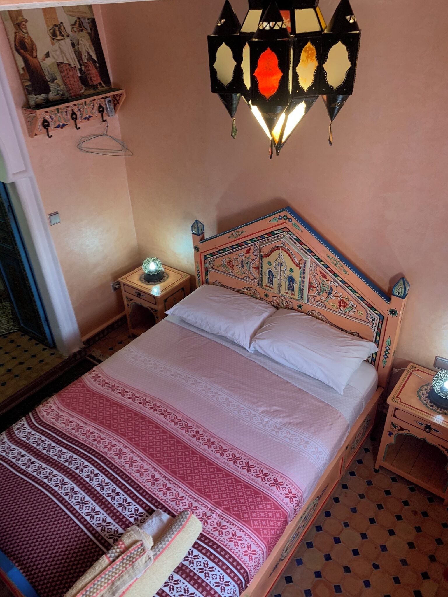 A bed with a patterned bedspread, a decorative headboard, and a wall-mounted light fixture.