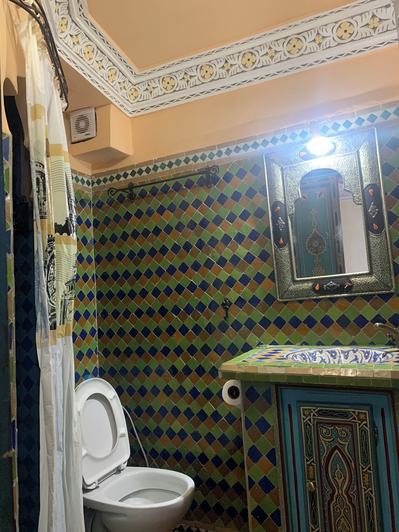 Une salle de bain avec un sol carrelé, des toilettes, un lavabo avec un récipient décoratif et un miroir avec un cadre ornemental.