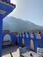 A terrace with a view of mountains, blue and white walls, and a tiled table with a bowl.
