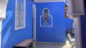 An archway leading to a courtyard with a blue wall, a tiled floor, and a small table with cushions.
