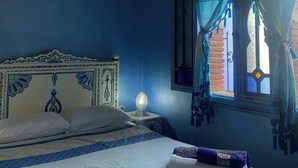 A bedroom with a bed, a nightstand, a wall-mounted lamp, and a window with curtains.