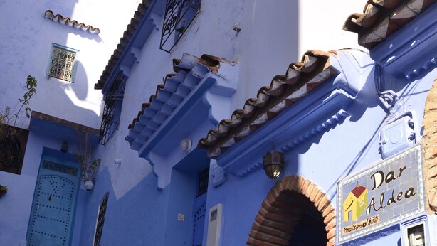 A narrow street with blue-painted buildings, a blue door, and a sign for 'Dar Aldea'.