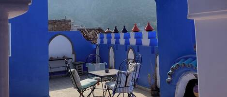Un patio con una mesa y sillas, piso de baldosas y vista a las montañas.