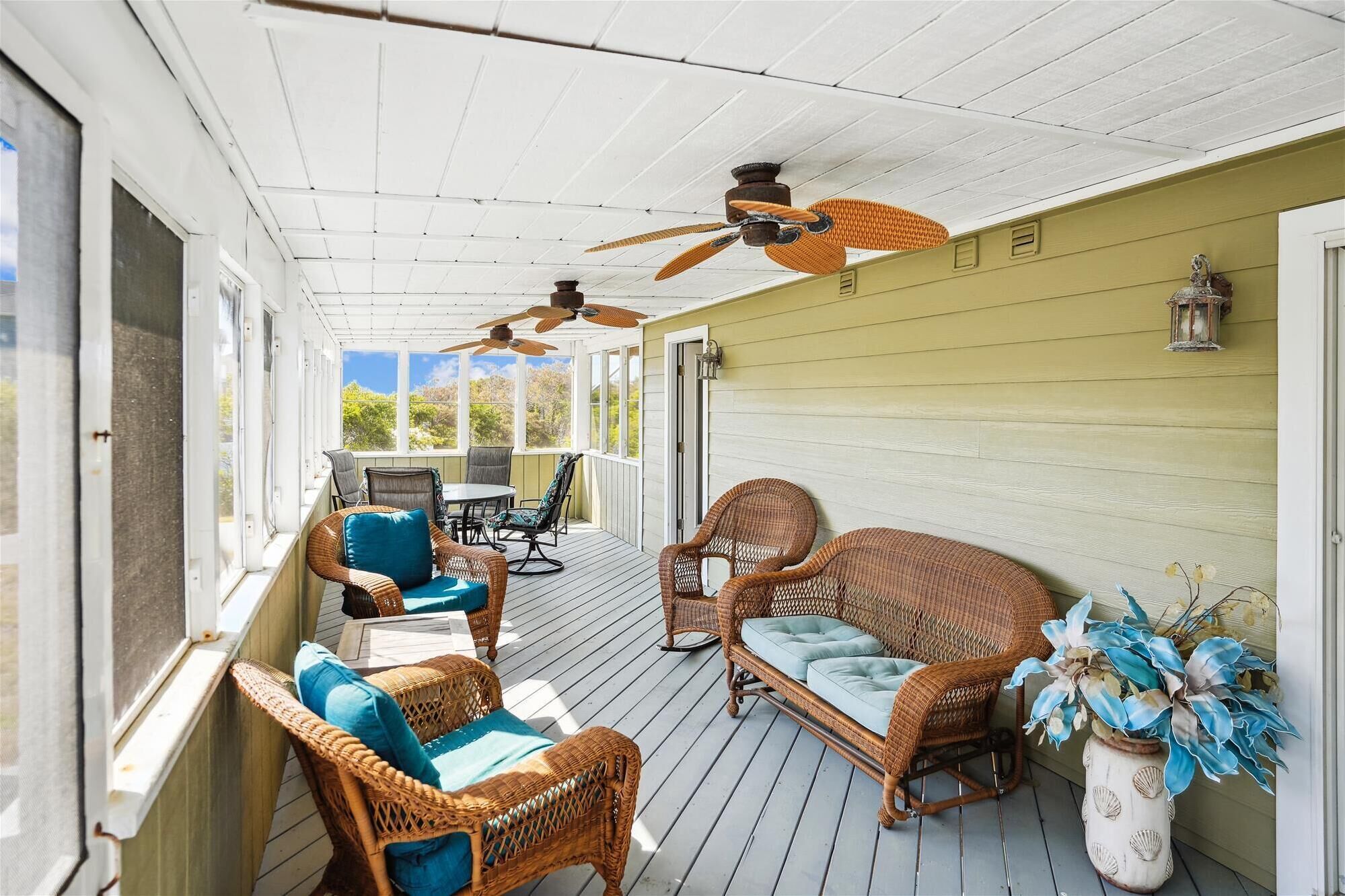 A covered porch with wicker furniture, ceiling fans, and a view of greenery.