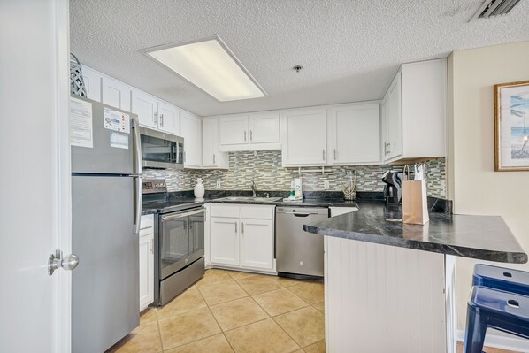 A modern kitchen with white cabinets, a stainless steel refrigerator, an oven, a dishwasher, and a tiled backsplash.