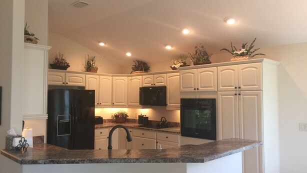 A kitchen with white cabinets, a granite countertop, a black refrigerator, a microwave, and a built-in oven.