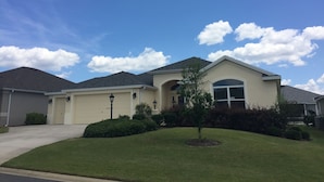 A residential house with a garage, a lawn, and a clear blue sky with clouds.