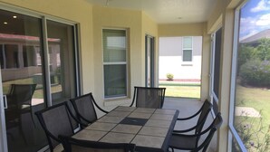 A covered patio area with a table and chairs, large sliding glass doors, and a view of a landscaped yard.