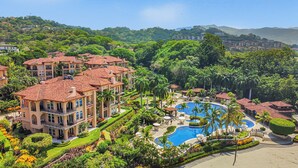 Un resort con una piscina grande, varias edificaciones y abundante vegetación.