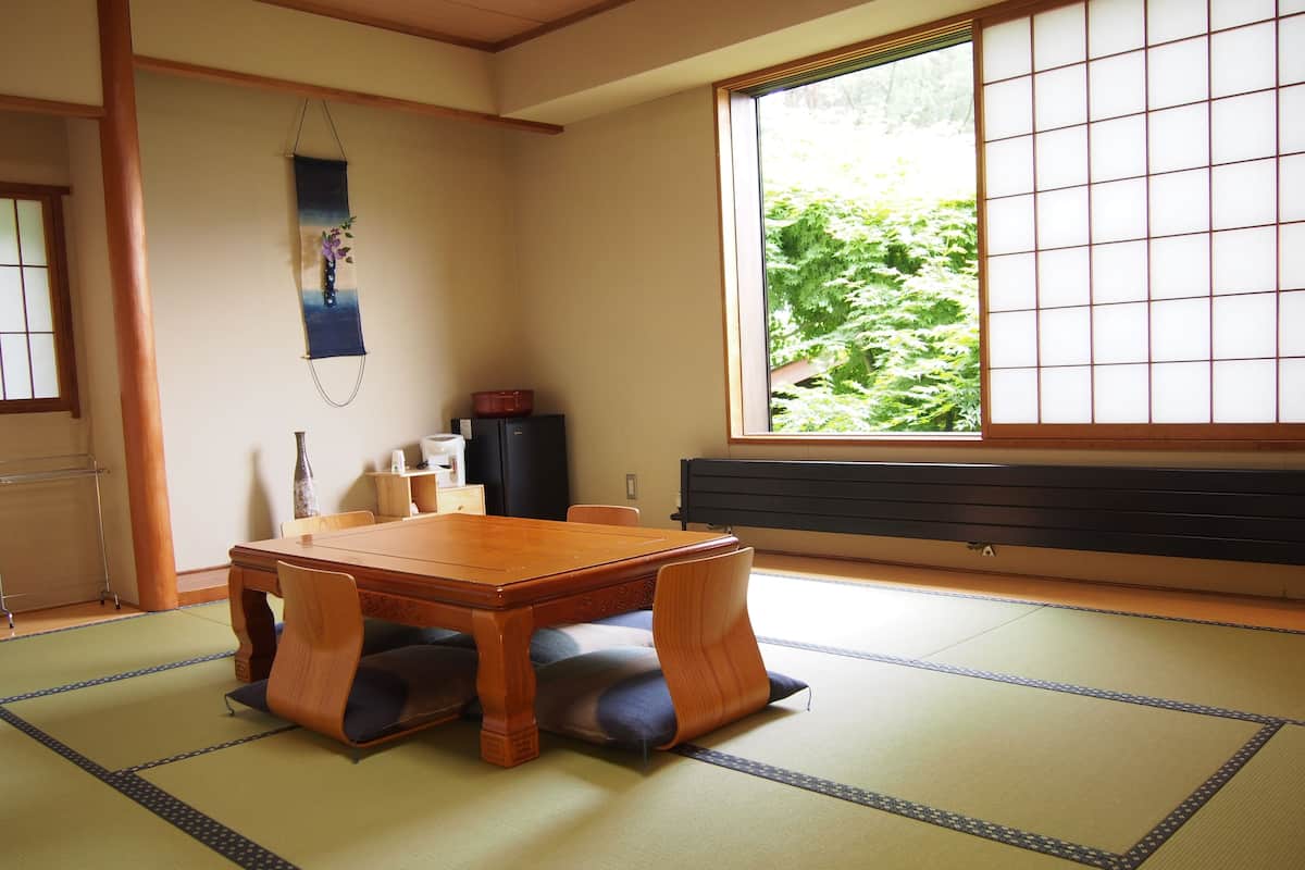 A traditional Japanese room with tatami flooring, a wooden table, and a sliding door with a view of greenery.