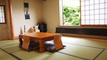 Una habitación japonesa tradicional con suelo de tatami, una mesa de madera y una puerta corredera con vistas a la vegetación.