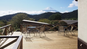 A wooden deck with chairs and a table, overlooking a mountain and forest. - Guesthouse Sakuya (Fujikawaguchiko)
