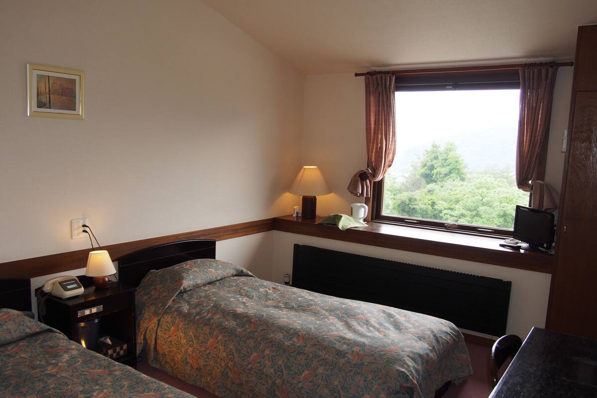 A hotel room with two beds, a desk, a computer, a window with curtains, and a painting on the wall.