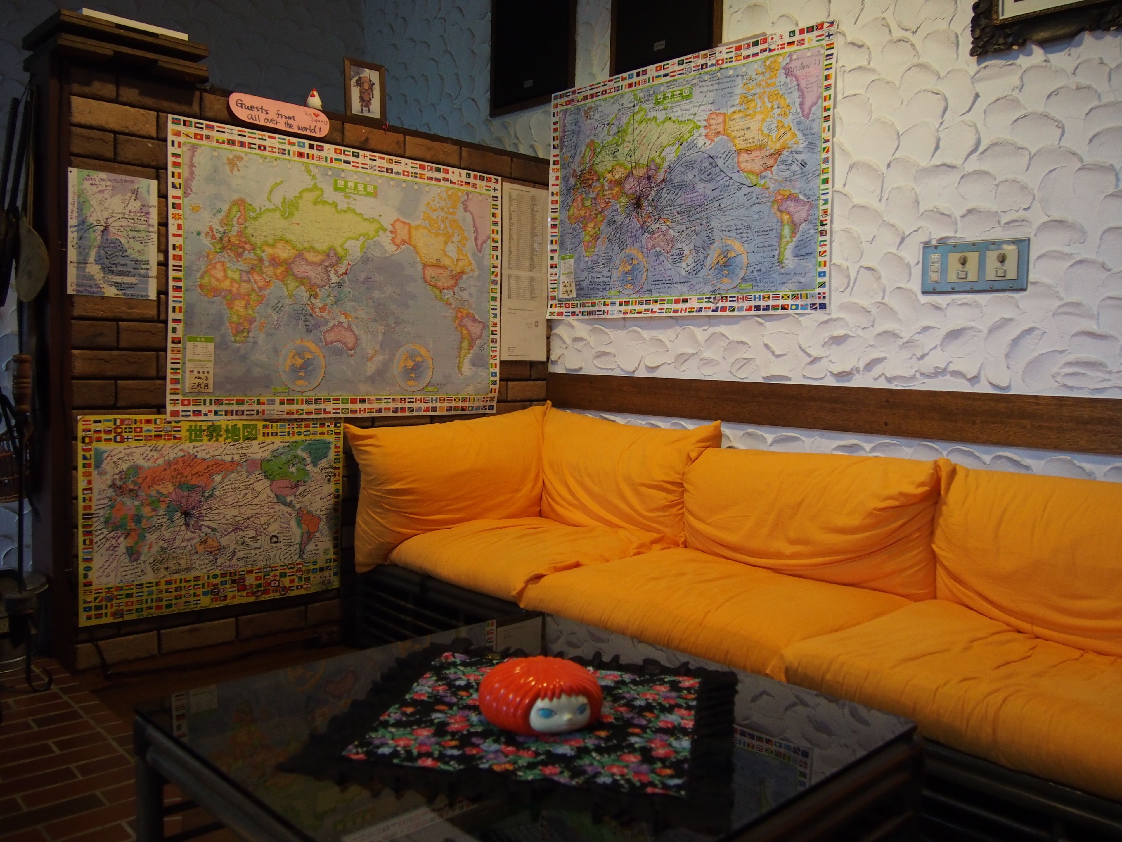 A room with a large world map on the wall, a bright orange sofa, and a glass coffee table with a decorative item.