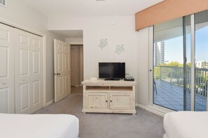 A hotel room with a balcony, a TV on a cabinet, and a door leading to another room. - Tile floors, spacious beachfront condo w/private balcony! (Destin)