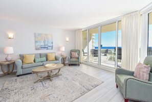 A spacious living room with a sofa, armchairs, a coffee table, and a painting of sailboats.