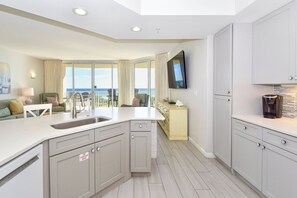 A modern kitchen with a central island, a dining area with a view, and a living space with a sofa and chairs.