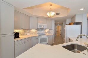 A modern kitchen with white cabinetry, a built-in microwave, a stainless steel sink, and a chandelier. - Tile floors, spacious beachfront condo w/private balcony! (Destin)