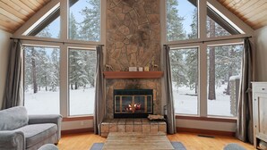 A cozy room with a stone fireplace, large windows, and a wooden ceiling.