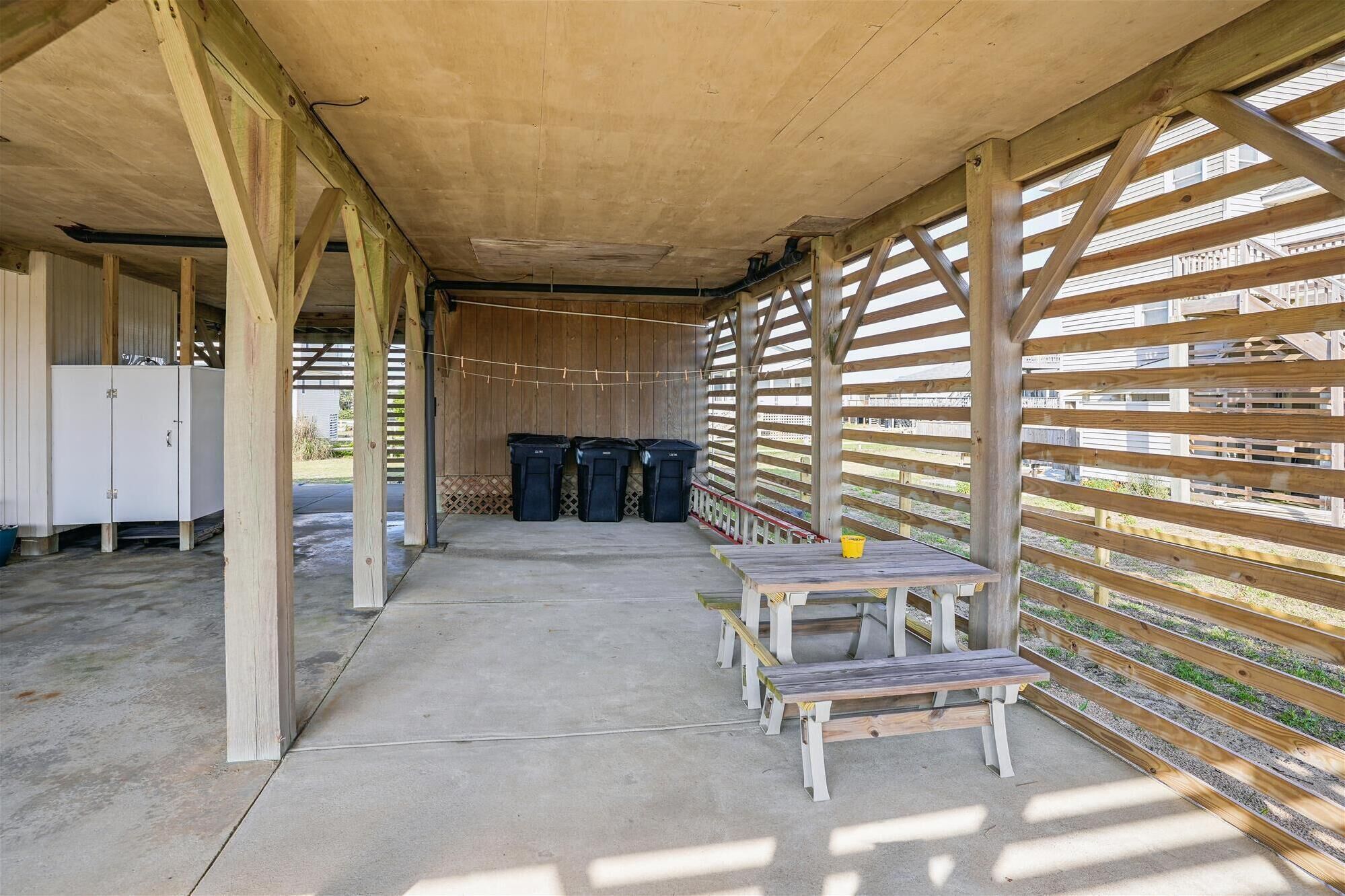 A covered outdoor area with wooden benches and trash bins.