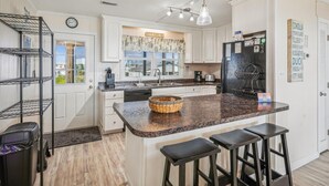 Una cocina con armarios blancos, encimera de granito, refrigerador negro y lámpara colgante.