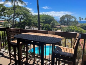 A wooden deck with a table and chairs, overlooking a swimming pool and lush greenery.