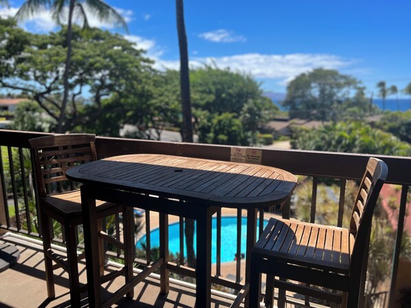 A wooden deck with a table and chairs, overlooking a swimming pool and lush greenery.