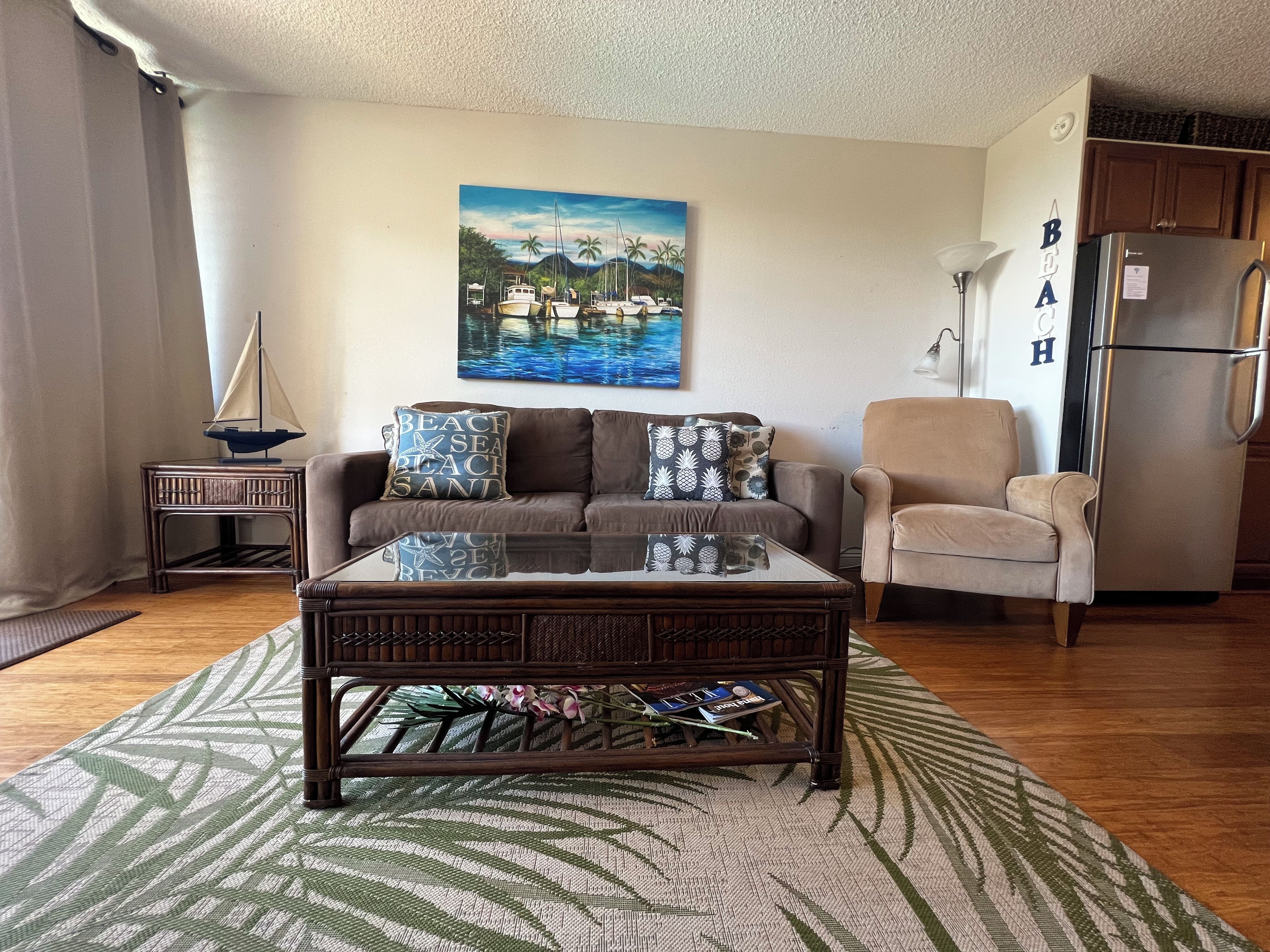 A living room with a sofa, armchair, coffee table, and a painting of a beach scene.