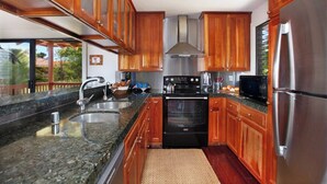A kitchen with wooden cabinets, stainless steel appliances, granite countertops, and a large window. - Makanui 111 walk to  Grand Hyatt By Suite Paradise (Koloa)