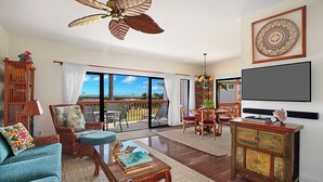 A spacious living room with a large window, a ceiling fan, and a television. - Makanui 111 walk to  Grand Hyatt By Suite Paradise (Koloa)