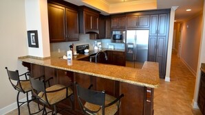 A kitchen with dark wood cabinets, a granite countertop, and a central island with bar stools. - Oasis, Formerly Phoenix West II, Beach front, Lazy River/Water Slide!! (Orange Beach)