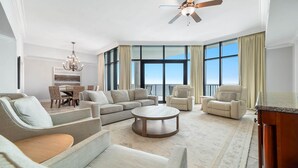 A spacious living room with a large window, a ceiling fan, and a dining area with wicker chairs. - Oasis, Formerly Phoenix West II, Beach front, Lazy River/Water Slide!! (Orange Beach)