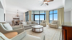 A spacious living room with a large window, a ceiling fan, and a dining area with wicker chairs.