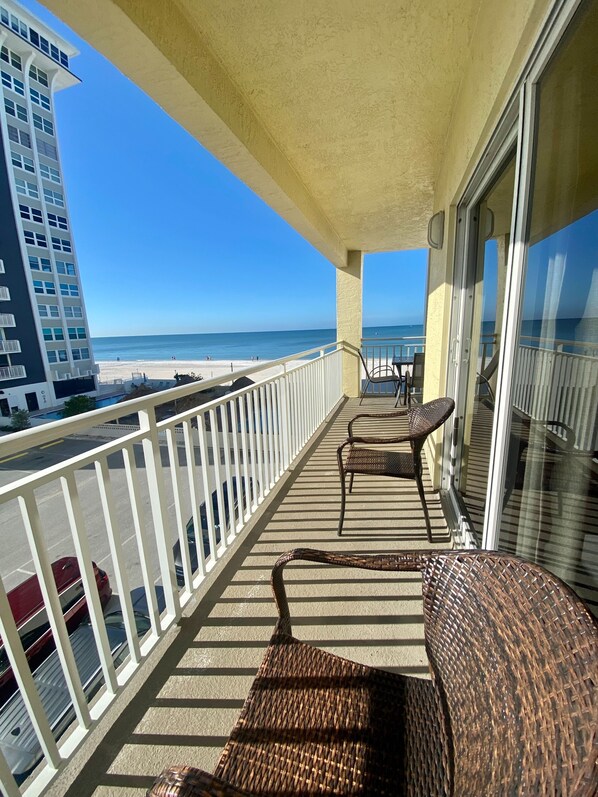 A balcony with wicker furniture, a view of the beach, and a tall building in the background.