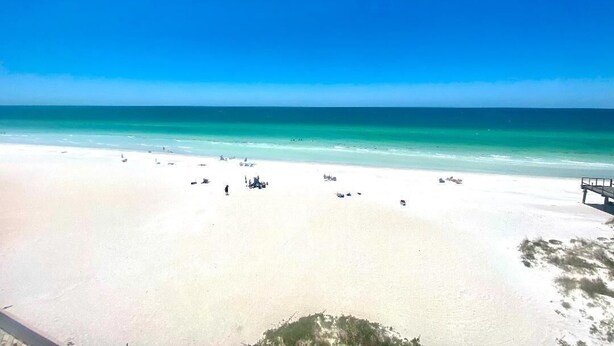 Una playa con agua turquesa cristalina, arena blanca y algunos objetos dispersos.