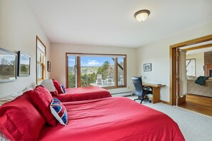 A bedroom with two beds, a desk, and a chair. There is a large window with a view of trees and hills. - Mountain Dream: 4 br, fireplace, a/c, game room, deck, hot tub, views! (Stowe)