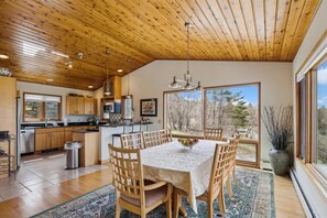 A spacious kitchen with wooden cabinets, a large island, and a dining area with a table and chairs. - Mountain Dream: 4 br, fireplace, a/c, game room, deck, hot tub, views! (Stowe)