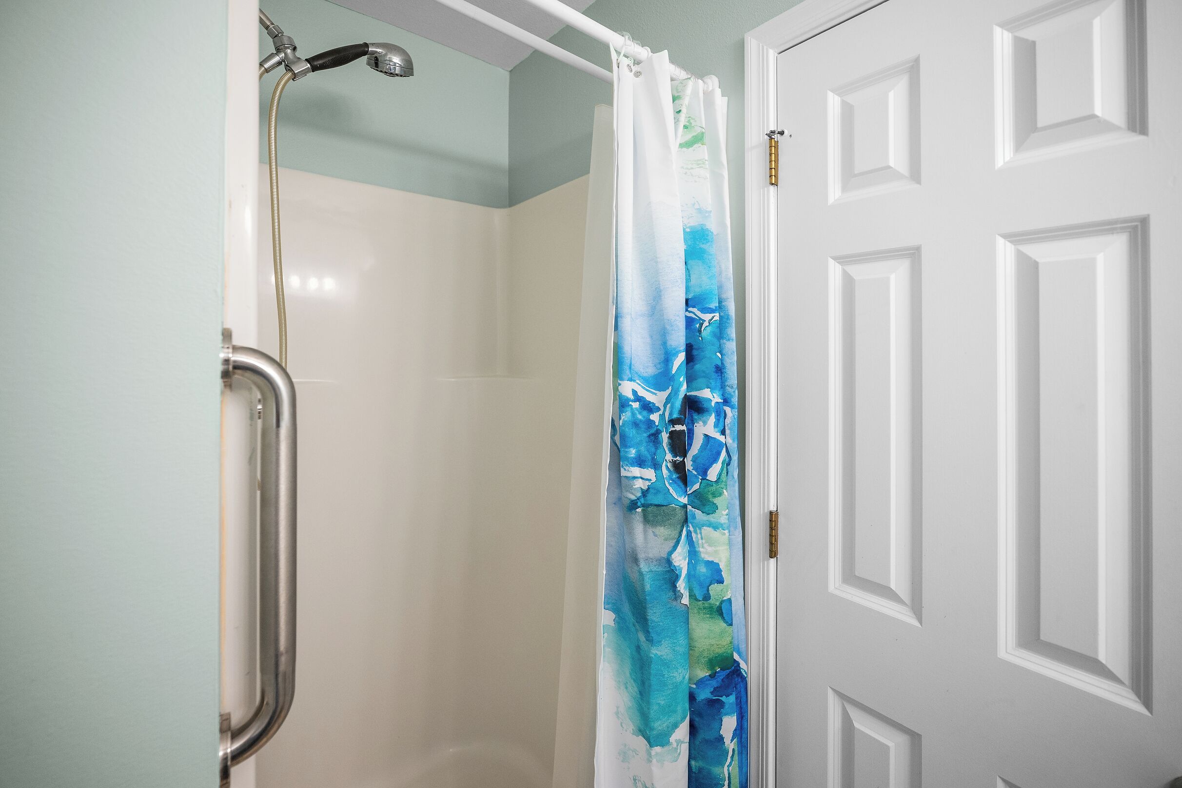 A shower with a white door and a blue and white shower curtain.