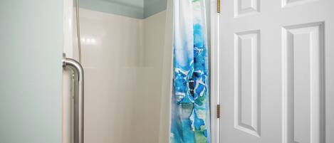 A shower with a white door and a blue and white shower curtain.