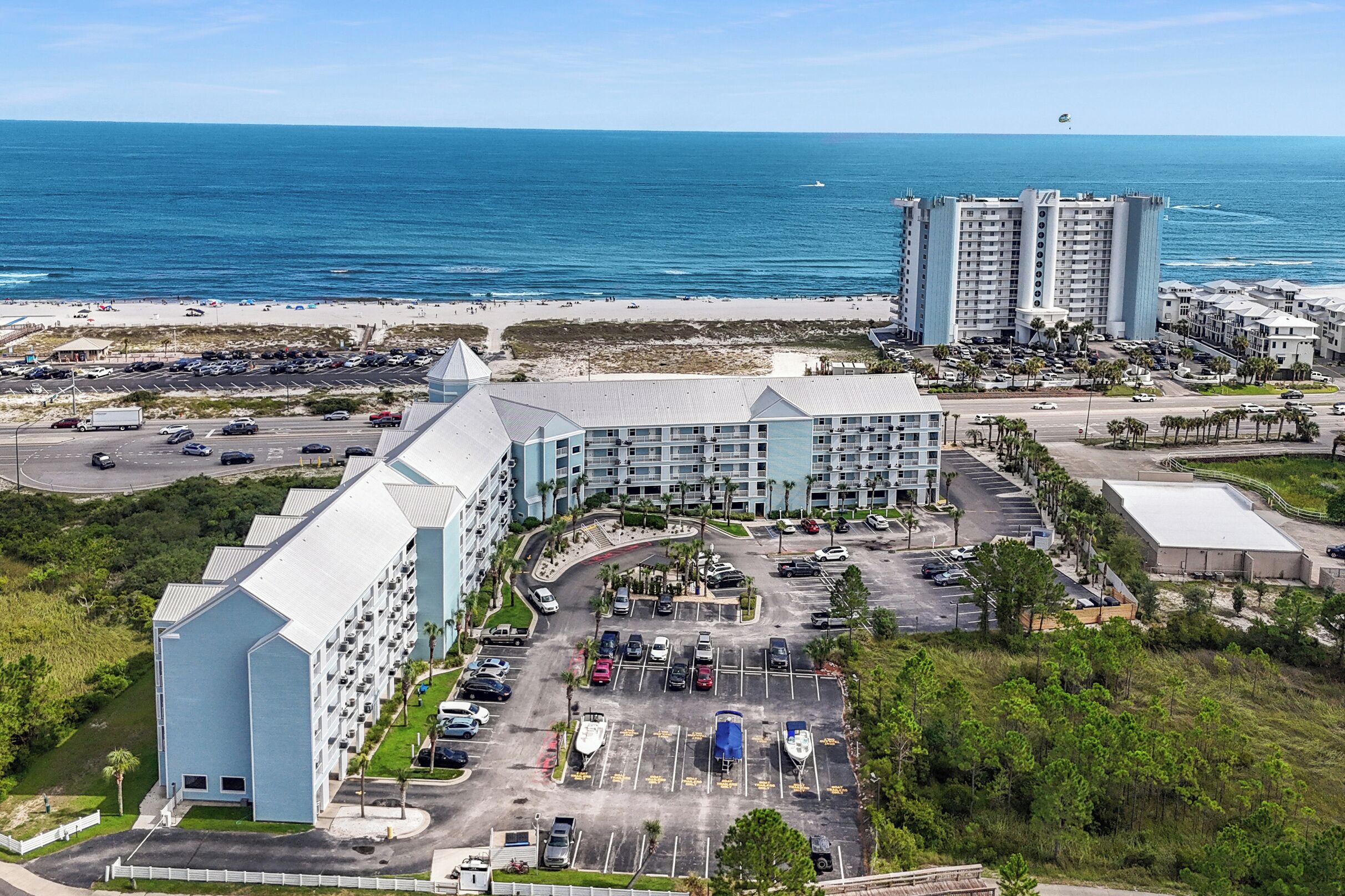 A hotel with a parking lot, a beach view, and a large building in the background.