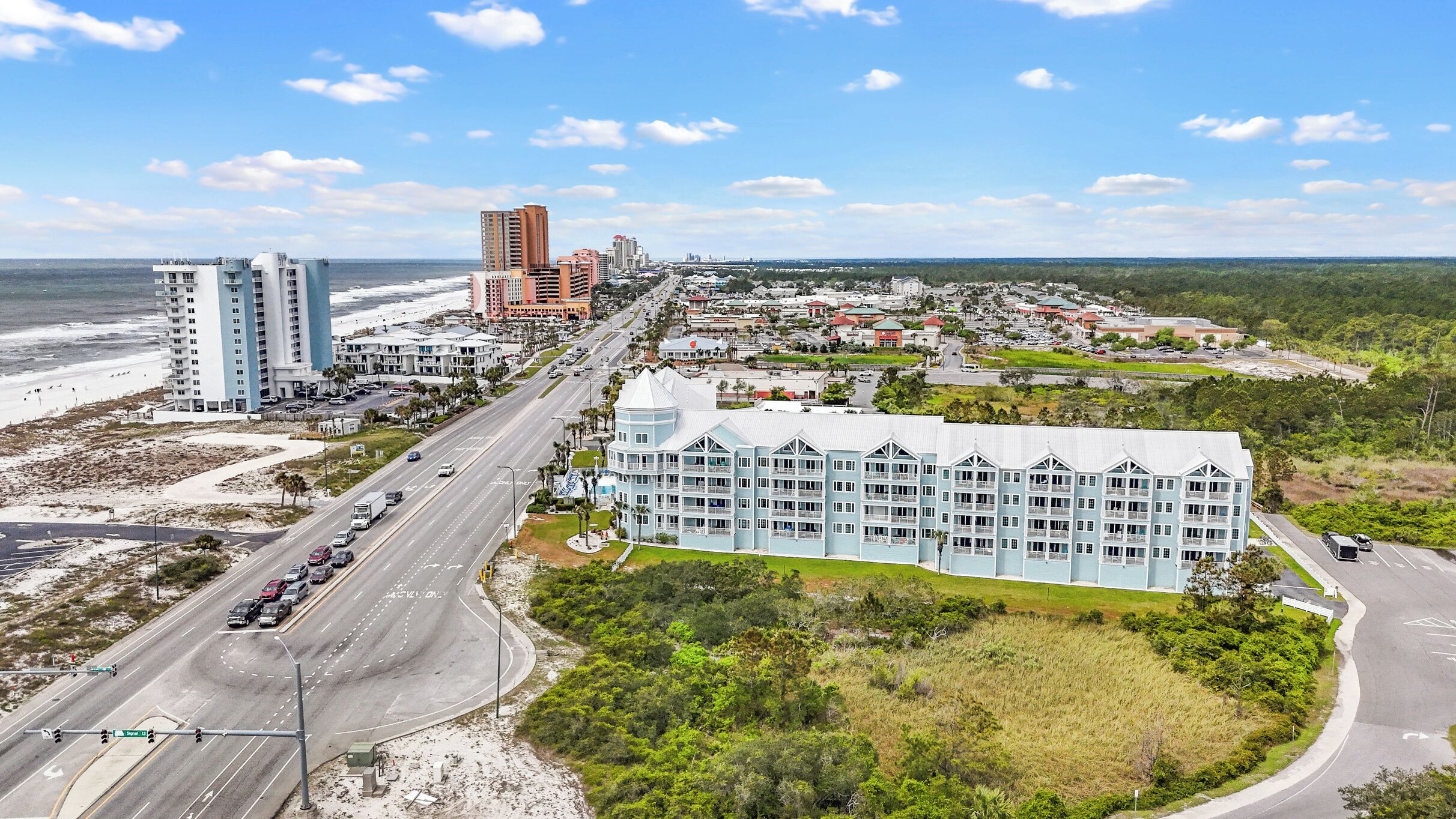A coastal hotel with multiple floors, a beachfront view, and a road leading to the beach.
