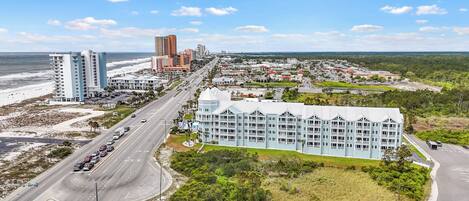 A coastal hotel with multiple floors, a beachfront view, and a road leading to the beach.