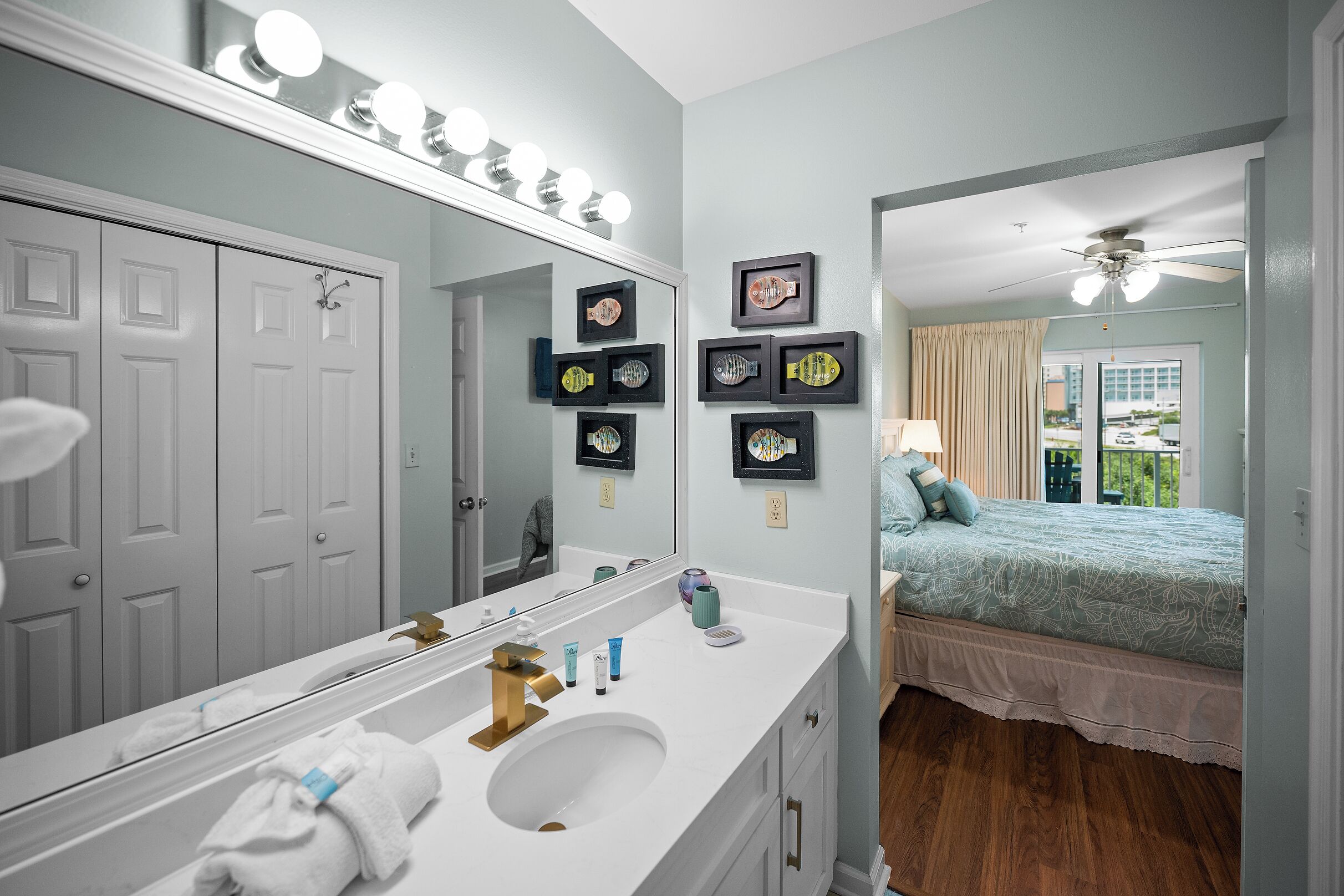 A bathroom with a large mirror, vanity, and a bed with a view.