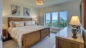 Une chambre avec un grand lit, une table de chevet, un bureau avec une lampe, une fenêtre donnant sur un beau paysage et deux tableaux représentant des oiseaux, accrochés au mur.