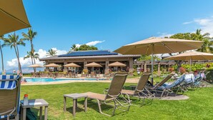 A poolside area with lounge chairs, umbrellas, and a building with a blue roof.