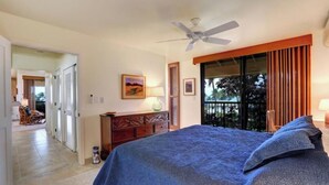 A bedroom with a bed, a ceiling fan, a nightstand, a lamp, a painting, and a view through a window.