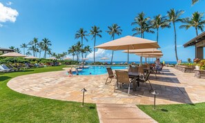 A poolside area with lounge chairs, umbrellas, and a view of the ocean.